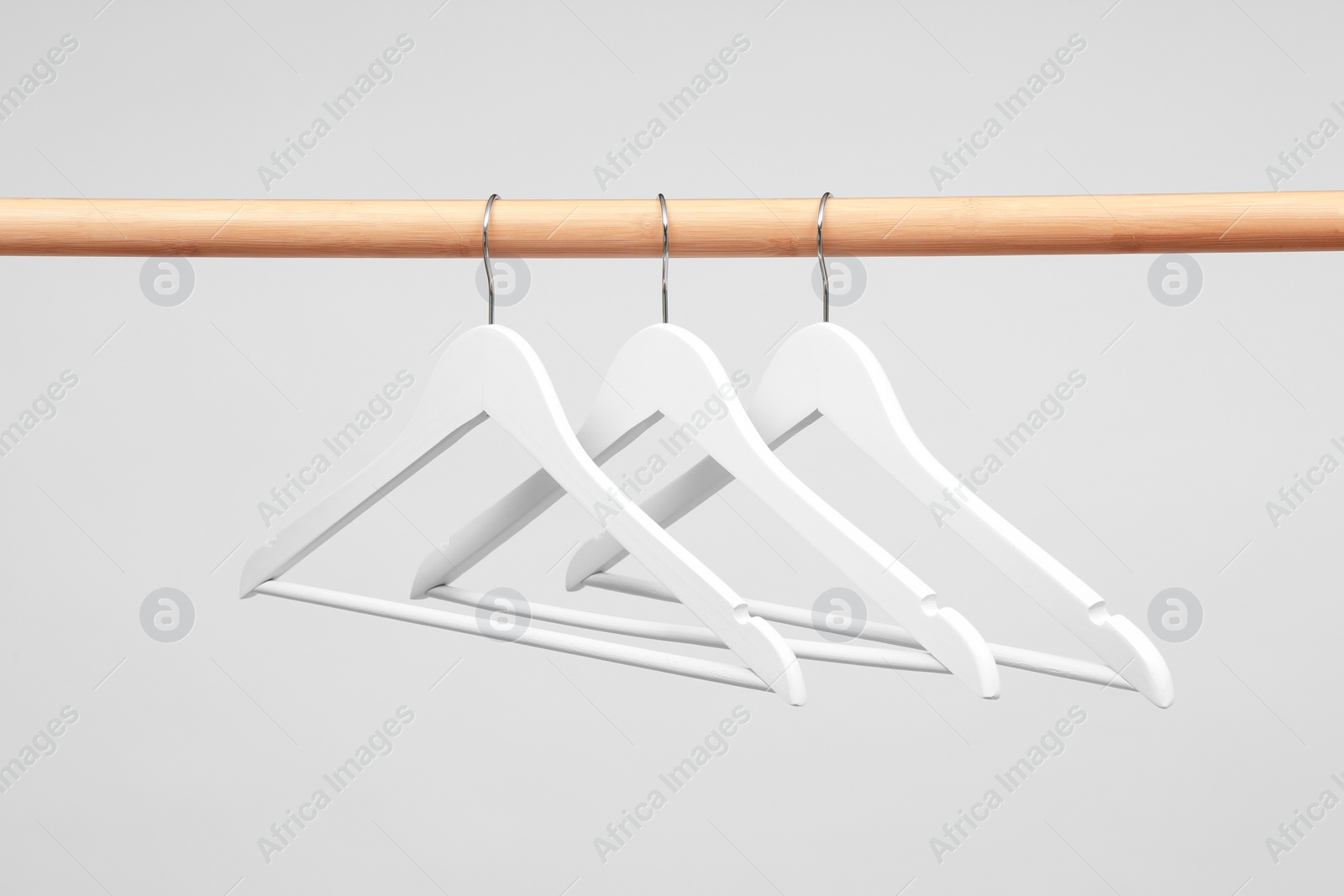 Photo of Empty clothes hangers on wooden rail against light background