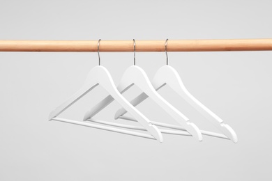 Photo of Empty clothes hangers on wooden rail against light background