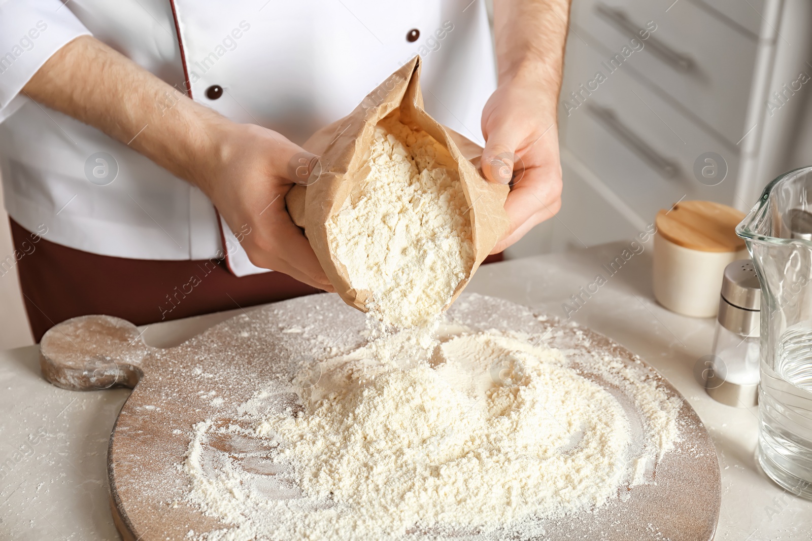 Photo of Male chef emptying flour out of paper package on board in kitchen