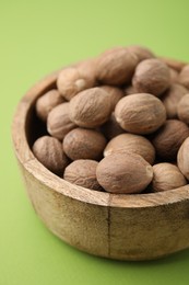 Photo of Whole nutmegs in bowl on light green background, closeup