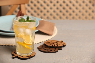 Glass of lemonade and leaf shaped cup coasters on grey wooden table