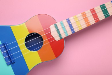 Photo of Colorful ukulele on pink background, top view. String musical instrument