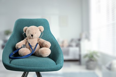 Teddy bear with stethoscope in armchair indoors, space for text. Pediatrician practice