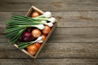 Photo of Crate with different kinds of onions on wooden table, top view. Space for text