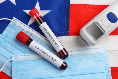Photo of Test tubes with blood samples, medical masks and thermometer on American flag, flat lay. Coronavirus pandemic in USA
