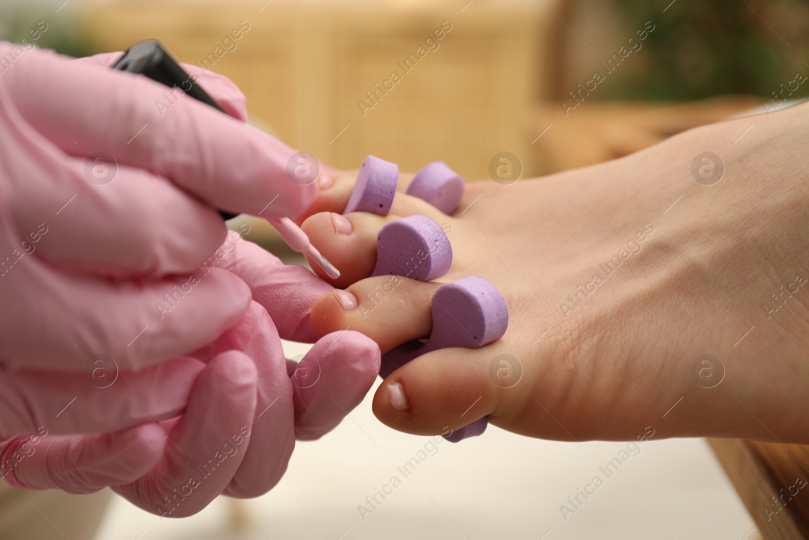 Photo of Professional pedicurist painting client`s toenails with polish in beauty salon, closeup