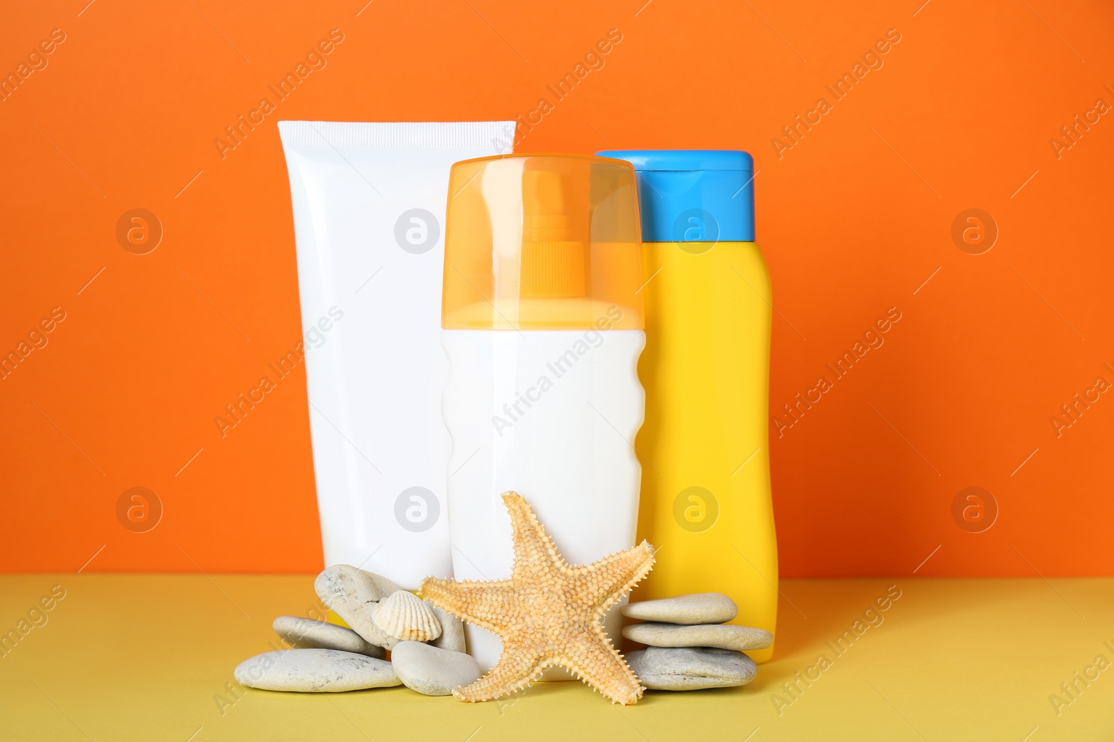 Photo of Different suntan products, starfish and stones on color background