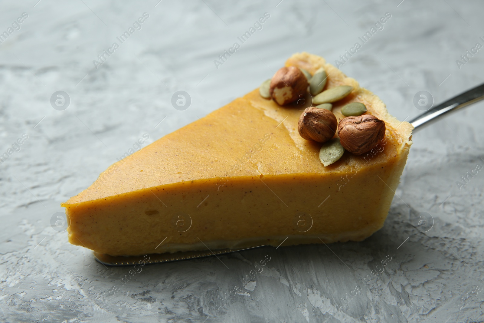 Photo of Cake server with piece of delicious pie with hazelnuts and pumpkin seeds on grey textured table, closeup