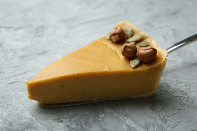 Cake server with piece of delicious pie with hazelnuts and pumpkin seeds on grey textured table, closeup