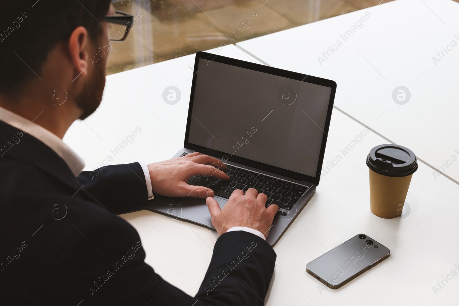 Photo of Man working on laptop at white desk in office, closeup