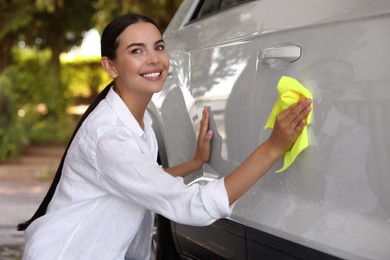 Photo of Happy woman cleaning car door with rag outdoors