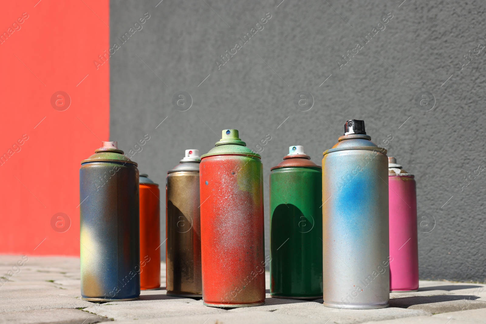 Photo of Cans of different spray paints on pavement near wall