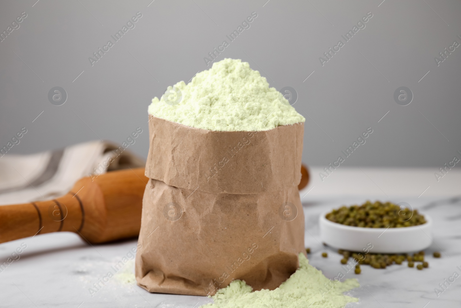 Photo of Mung bean flour in paper bag and seeds on white marble table