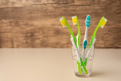 Photo of Toothbrushes in glass on beige table. Space for text
