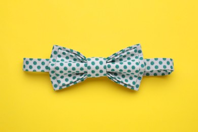 Photo of Stylish bow tie with green polka dot pattern on yellow background, top view