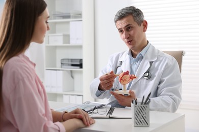 Gastroenterologist with human stomach model consulting patient at table in clinic