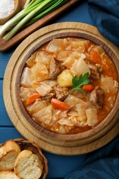 Photo of Tasty cabbage soup with meat, carrot and parsley served on blue wooden table, flat lay