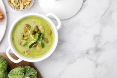 Delicious broccoli cream soup with pumpkin seeds on white marble table, flat lay. Space for text