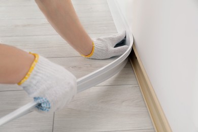 Man installing plinth on laminated floor in room, closeup