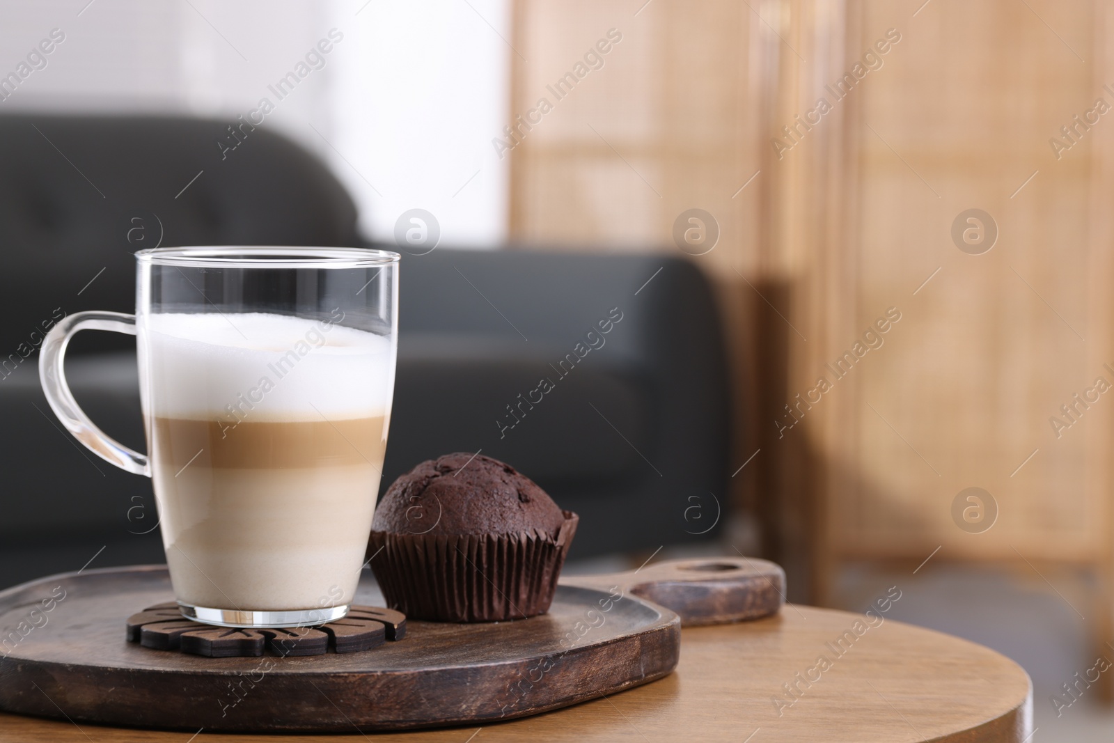 Photo of Cup of aromatic latte macchiato and chocolate muffin on wooden table against blurred background. Space for text