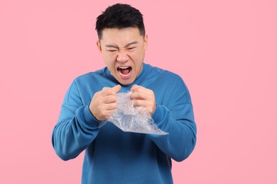 Emotional asian man with bubble wrap on pink background