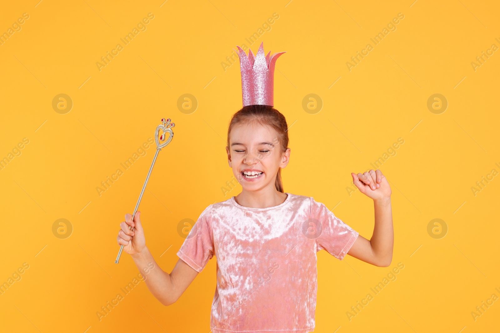 Photo of Cute girl in pink crown with magic wand on yellow background. Little princess