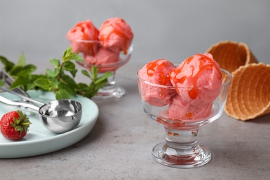 Photo of Delicious pink ice cream served with syrup in dessert bowl on grey table