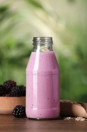 Photo of Delicious blackberry smoothie in glass bottle, oatmeal and berries on wooden table