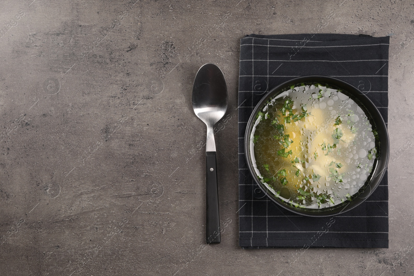 Photo of Delicious chicken soup with parsley and spoon on grey table, flat lay. Space for text