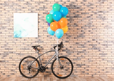 Bicycle with colorful balloons near brick wall indoors