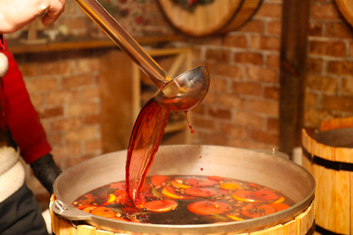 Photo of Seller pouring tasty aromatic mulled wine at winter fair, closeup