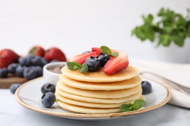 Photo of Delicious pancakes with strawberries, blueberries and chocolate sauce on light table, closeup