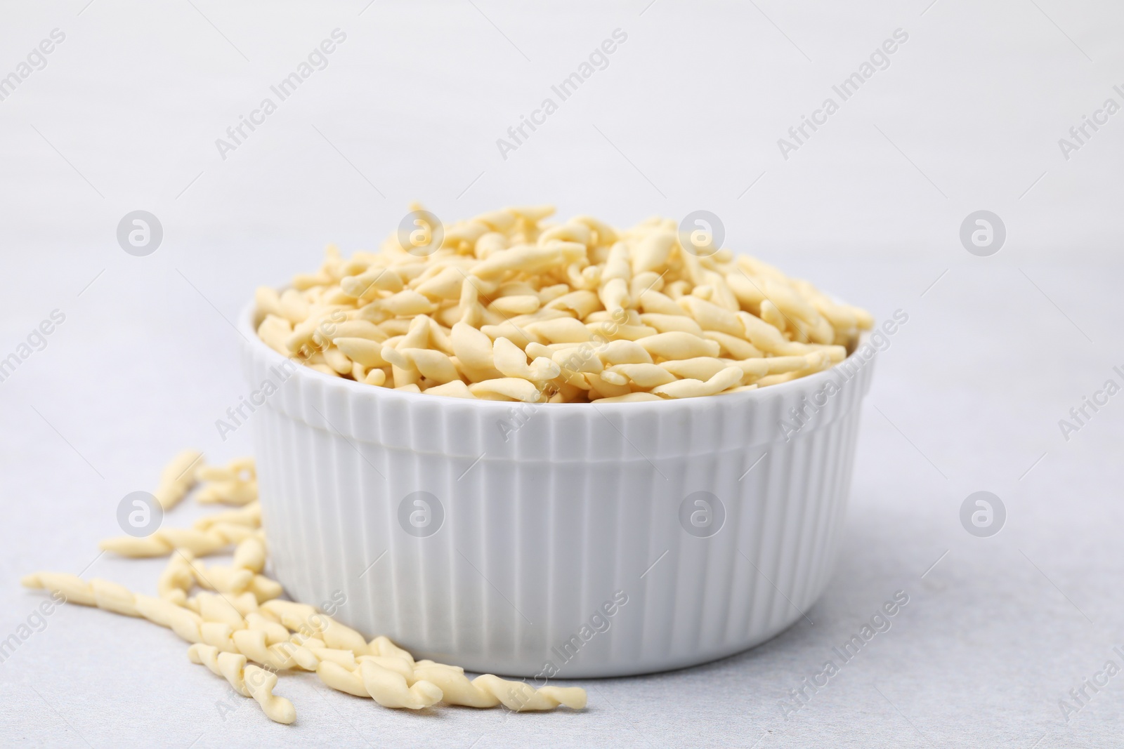 Photo of Bowl with uncooked trofie pasta on light grey table, closeup