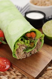 Delicious tortilla wrap with tuna on wooden board, closeup