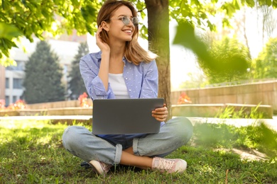 Image of Happy young woman with laptop sitting on green grass in park