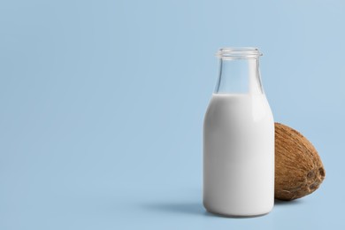 Photo of Glass bottledelicious vegan milk and coconut on light blue background, space for text