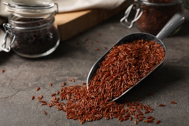 Photo of Uncooked brown rice in metal scoop on table. Space for text