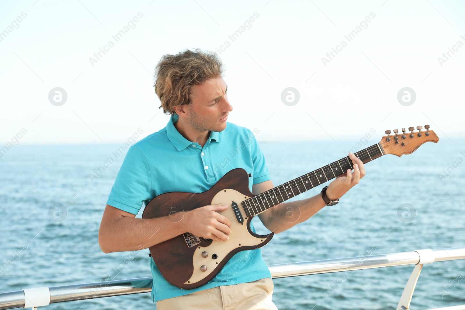 Photo of Portrait of handsome young man with guitar on sea pier