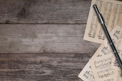 Photo of Sheets with musical notes and flute on wooden table, flat lay. Space for text