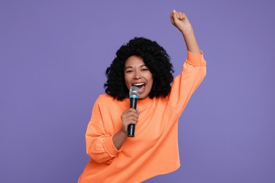 Beautiful woman with microphone singing on violet background