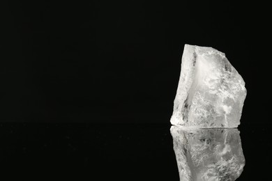 Photo of Piece of clear ice on black mirror surface, space for text