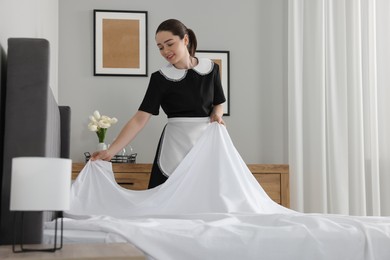 Young maid making bed in hotel room
