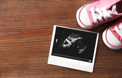 Ultrasound picture and baby shoes on wooden background, top view with space for text