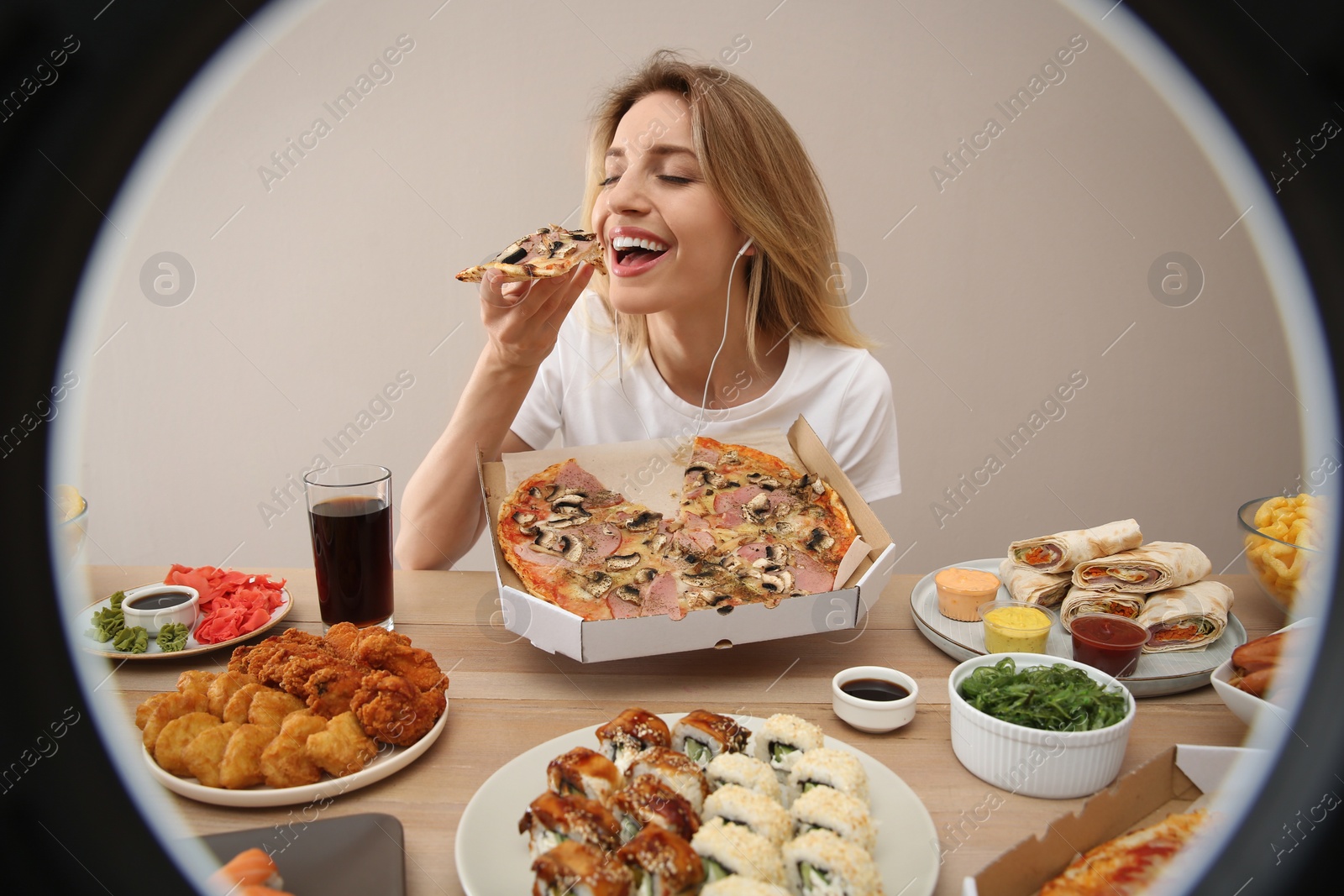 Photo of Food blogger eating at table against beige background, view through ring light. Mukbang vlog