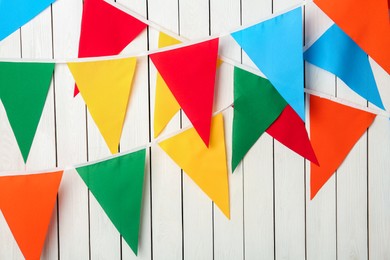 Buntings with colorful triangular flags hanging on white wooden wall. Festive decor