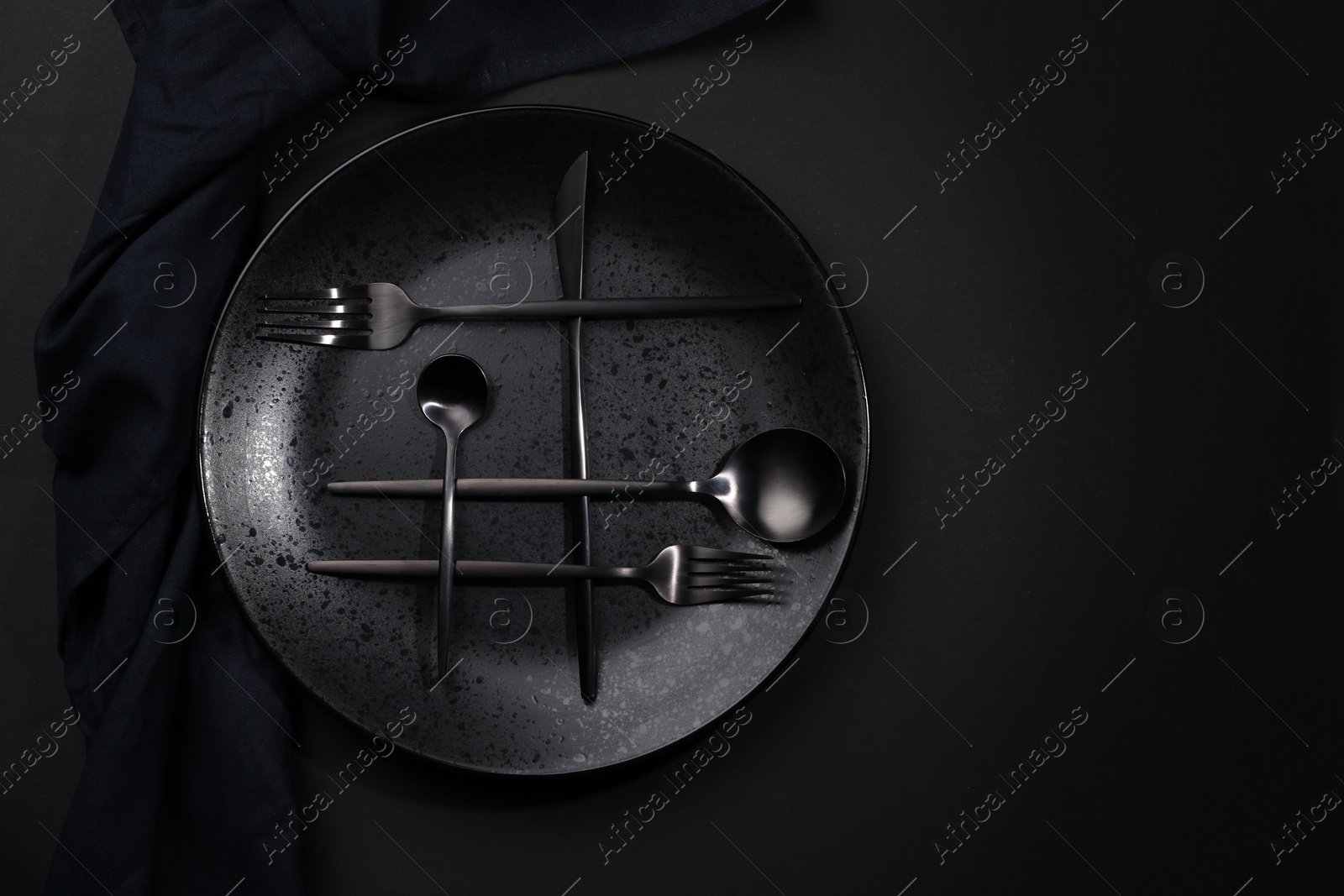 Photo of Stylish table setting. Plate, napkin and cutlery on black background, top view with space for text