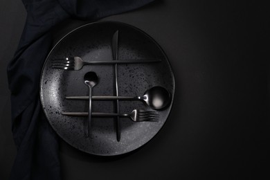 Stylish table setting. Plate, napkin and cutlery on black background, top view with space for text