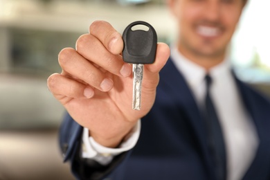 Photo of Young salesman with car key in modern dealership, focus on hand