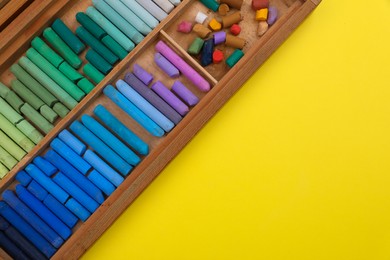 Photo of Set of soft pastels in wooden box on yellow background, top view with space for text. Drawing material