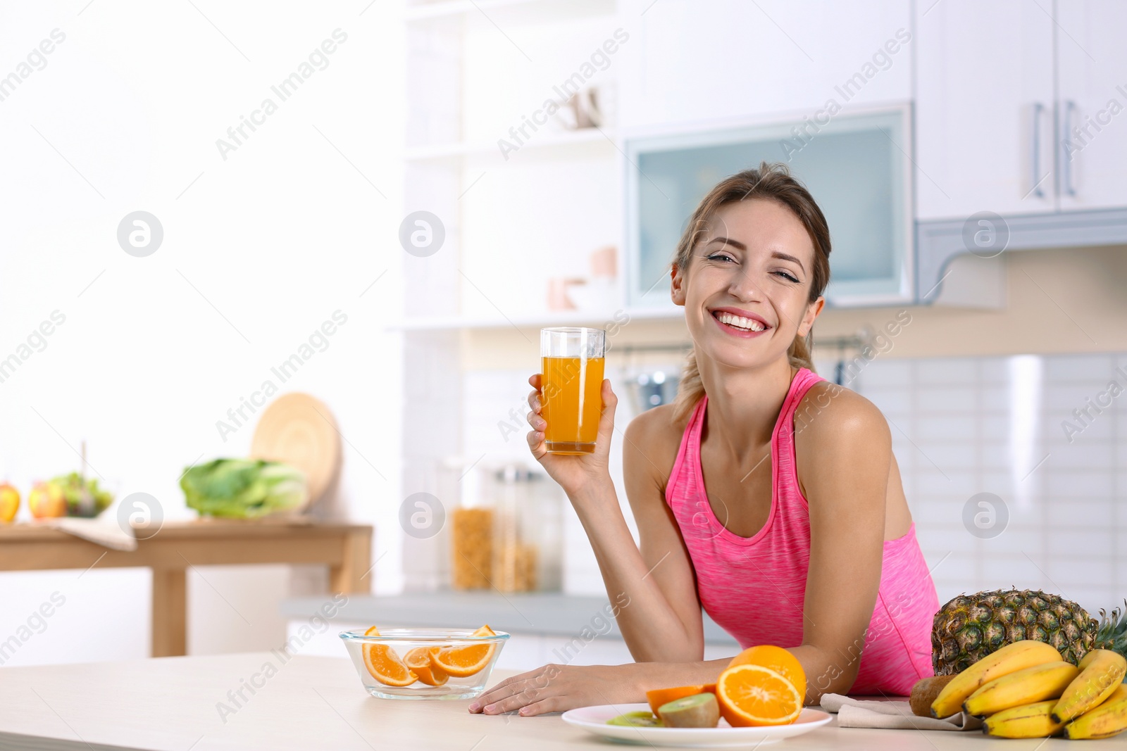 Photo of Woman with glass of orange juice at table in kitchen. Healthy diet